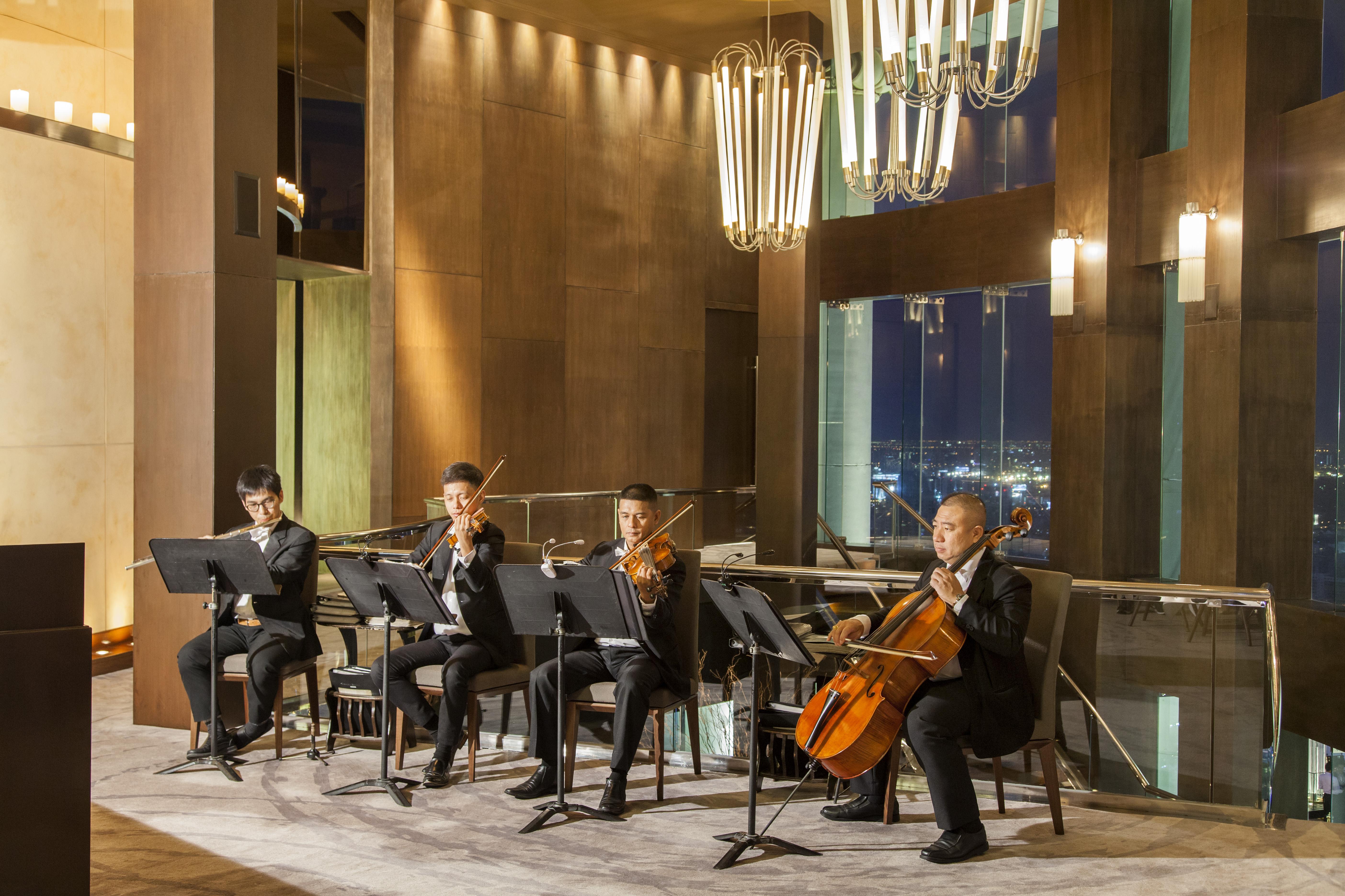 Lebua At State Tower Hotel Банкок Екстериор снимка The photo shows a string quartet performance taking place in a sophisticated indoor setting. Four musicians are seated, each playing a different string instrument: two are playing violins, one is playing a viola, and one is playing a cello. They are 